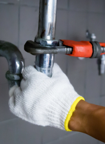Gloved hand using wrench on pipe